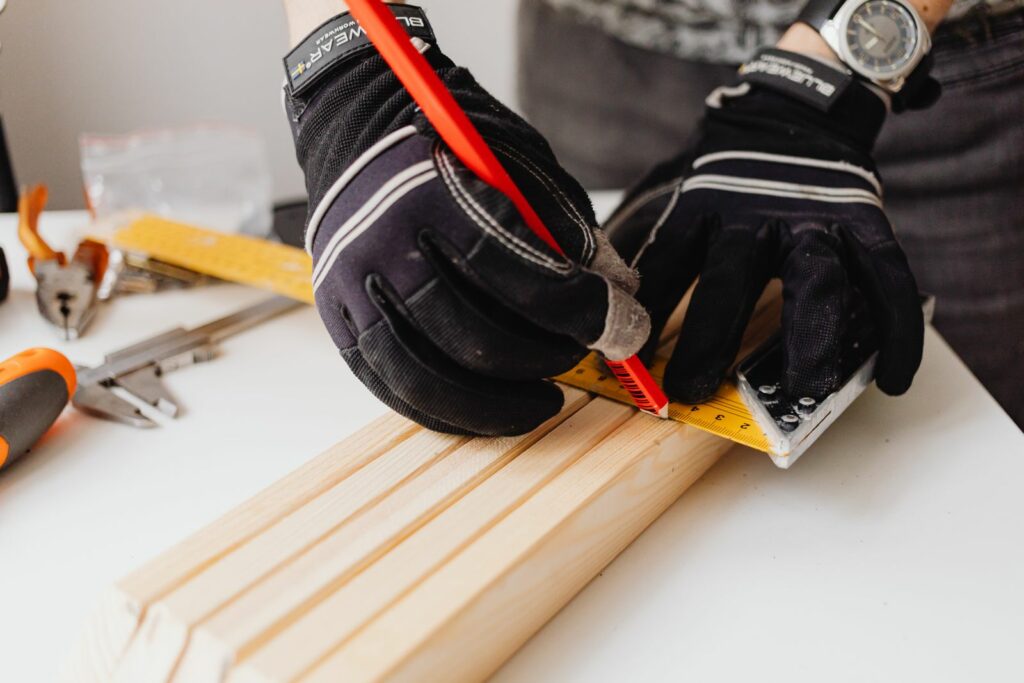 Gloved hands marking a length of timber trim with a tape measure