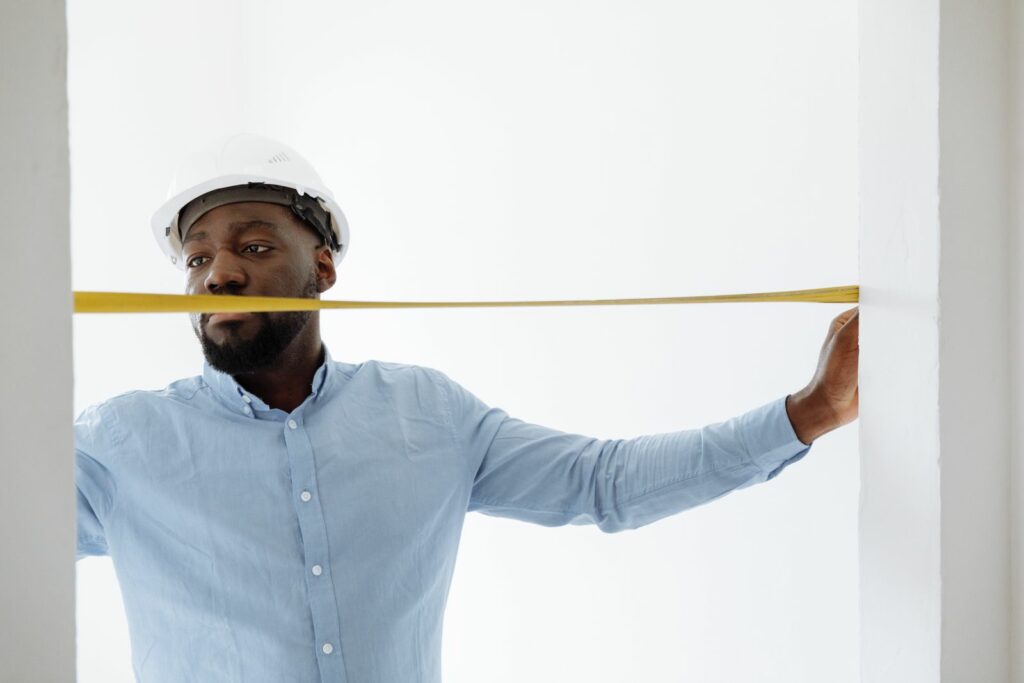 A person in a hard hat measuring a wall with a tape measure